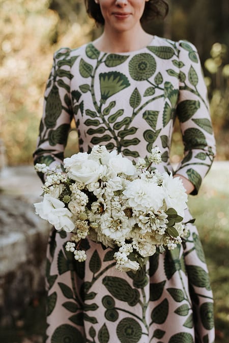 A micro wedding bride in a floral dress holding a green and white modern bridal bouquet of zinnias, garden roses, and berries designed by Nectar and Root, Vermont wedding florist at the Marble House Project in Dorset, Vermont.