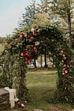 Lush romantic fall outdoor ceremony arbor of September cafe au lait dahlias, garden roses, and hanging amaranth in a burgundy and rust color palette decorated by Nectar and Root, Vermont wedding florist at Edson Hill in Stowe, Vermont.
