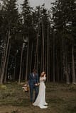 Bride and groom standing at the edge of a forest tree line, holding a fall September bridal bouquet by Nectar and Root, Vermont wedding florist at Edson Hill in Stowe, Vermont.
