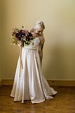 A boho bride wearing a beaded white wedding dress holding a fall bridal bouquet of September dahlias, hydrangea, and fall foliage in a burgundy and blush color palette with flowing hand dyed silk ribbons by Nectar and Root, Vermont wedding florist