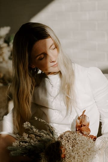 A bride holding a modern bridal fall bridal bouquet of dried flowers in a warm dusty neutral color palette in the sunshine by Nectar and Root, Vermont wedding florist.
