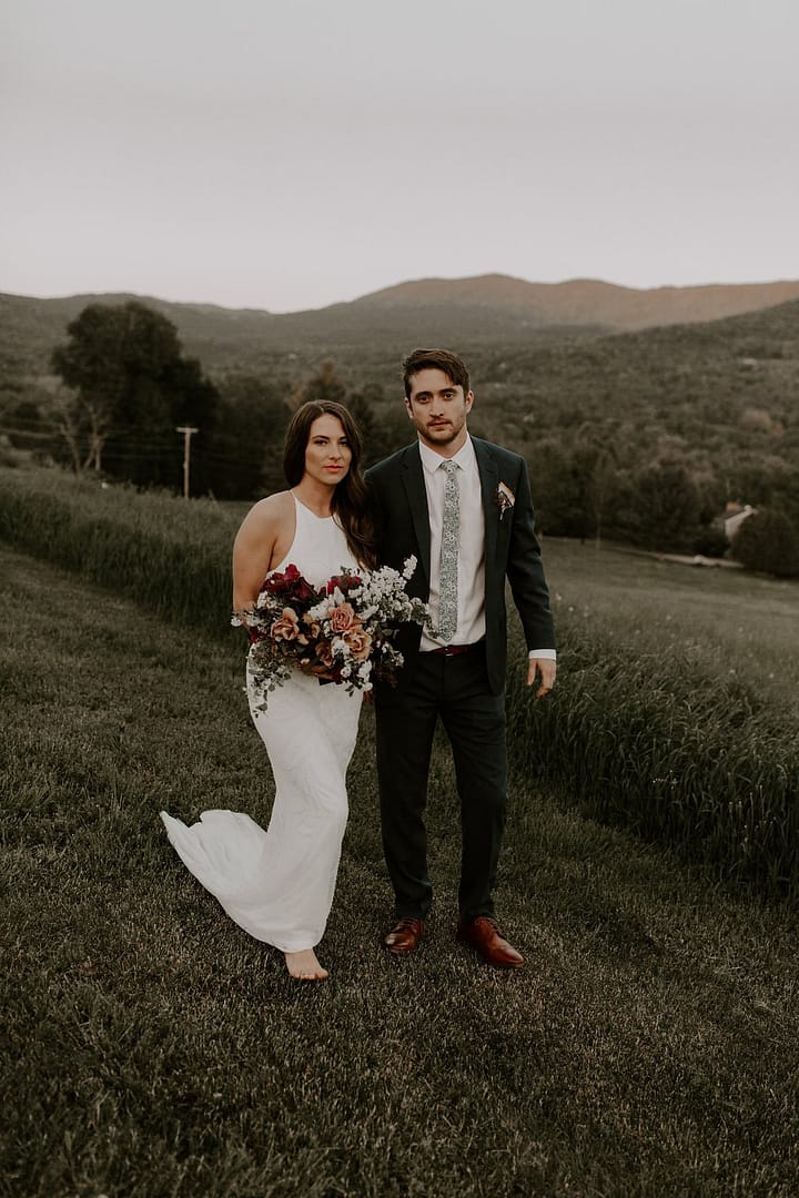 Outdoor elopement bride and groom with mountain views holding a peach, blush and burgundy bridal bouquet by Nectar and Root, Vermont wedding florist at a backyard wedding in Vermont.