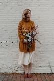 A bride standing outside holding a romantic fall bridal bouquet of October eucalyptus, mums, iris and hellebores in a moody blue color palette by Nectar and Root, Vermont wedding florist.