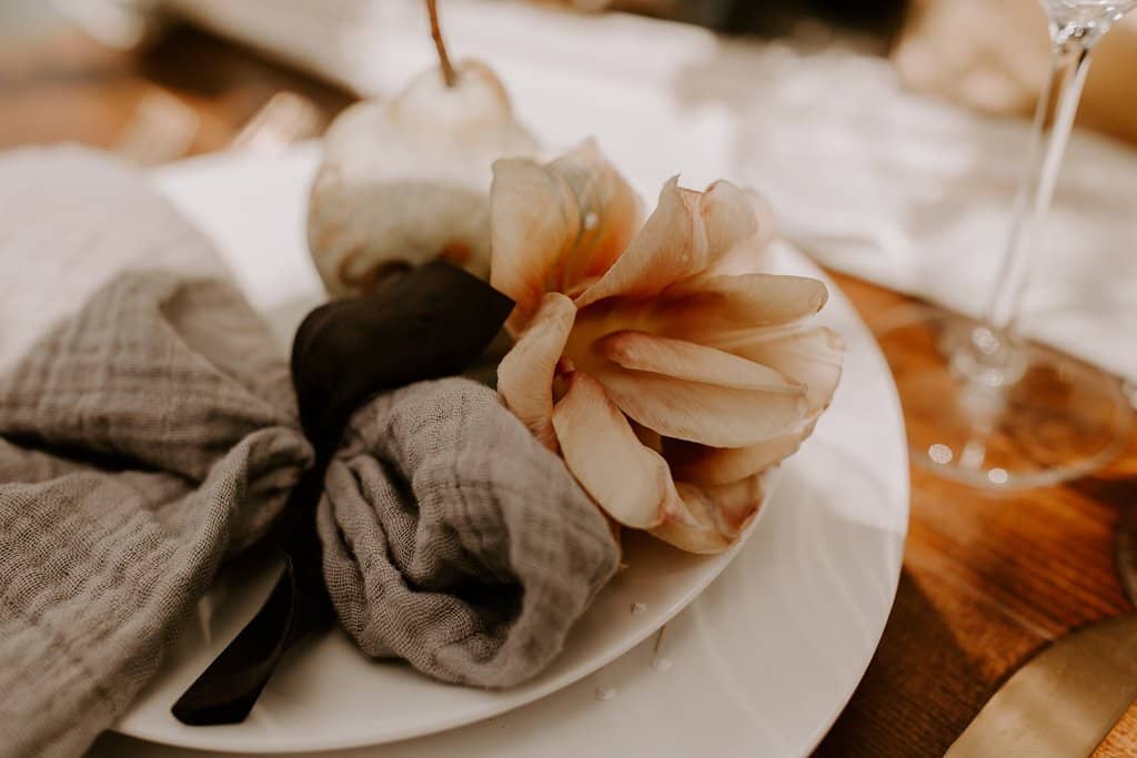 Artful napkin accent and place setting made of a hand dyed silk ribbon, cheesecloth napkin, belle epoque tulip and anjou pear in warm neutral tones for outdoor micro wedding by Nectar and Root, Vermont wedding florist at a backyard wedding in Vermont.