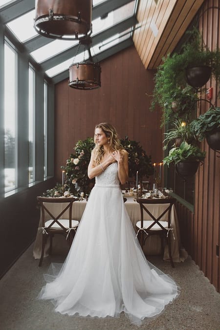 A bride standing in front of a lush indoor reception centerpiece designed by Nectar and Root, Vermont wedding florist at Trapp Family Lodge in Stowe, Vermont.