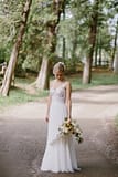Bride in white dress standing by trees with flower bouquet by Nectar and Root, Vermont wedding florist at Shelburne Coach Barn in Shelburne, Vermont.