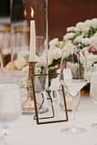 White centerpiece next to tapered candlesticks, gold candleholders and gold table number by Nectar and Root, Vermont wedding florist at Shelburne Coach Barn in Shelburne, Vermont.