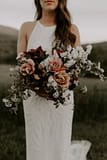 A boho peach, blush and burgundy June bridal bouquet of peonies, belle epoque tulips, garden roses, iris, and flowering branches with flowing silk ribbon by Nectar and Root, a Vermont wedding florist at a backyard micro wedding in Vermont.