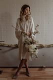 A bride standing inside wearing a simple modern silk wedding dress holding a spring bridal bouquet of May white flowering branches by Nectar and Root, Vermont wedding florist.