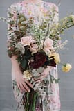 A bride wearing a floral dress holding a modern spring bridal bouquet of March fritillaria, flowering branches, eucalyptus, and garden roses in a pastel color palette by Nectar and Root, Vermont wedding florist in Brooklyn, New York.