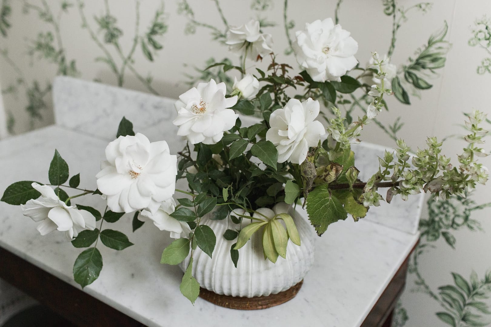 A simple summer reception centerpiece in a green and white neutral color palette atop a marble table with a marble vase featuring garden roses by Nectar and Root, Vermont wedding florist at Shelburne Museum in Shelburne, Vermont.