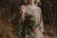 A bride wearing a khaki dress holding a simple fall bridal bouquet of October clematis, vines, wildflowers, jasmine and orchids in a warm neutral palette of rust, orange, and purple by Nectar and Root, Vermont wedding florist in Burlington, Vermont.