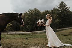 Bride standing beside a horse at an outdoor fall private estate reception venue holding a modern bridal bouquet by Nectar and Root, Vermont wedding florist at Edson Hill in Stowe, Vermont.