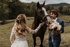 Bride and groom standing beside a horse at an outdoor fall private estate reception venue holding a modern bridal bouquet by Nectar and Root, Vermont wedding florist at Edson Hill in Stowe, Vermont.