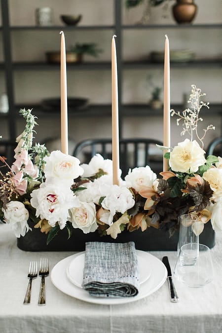 A modern summer reception centerpiece in a dusty neutral color palette atop an indoor reception table with linen napkins featuring garden roses, orchids, and foxglove by Nectar and Root, Vermont wedding florist.